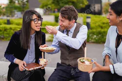Preview: Diverse young business people having fun eating together outside of office building