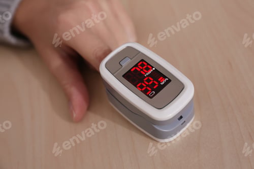 Preview: Woman measuring oxygen level with modern fingertip pulse oximeter at wooden table, closeup