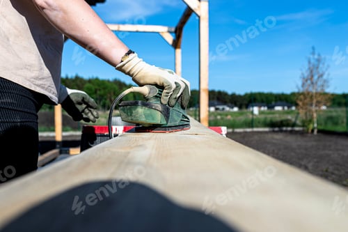 Preview: A woman sands a board with a small orbital sander placed on trestles in the garden.
