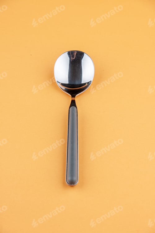 Preview: Vertical view of stainless teaspoon lying on golden background with free space