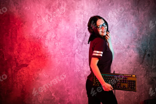 Preview: Female esports gamer posing with a gaming gear in neon light. Streamer girl standing with a gaming