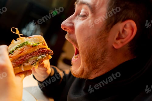 Preview: close-up man with enjoy biting delicious juicy cheeseburger in cafe restaurant junk food calories