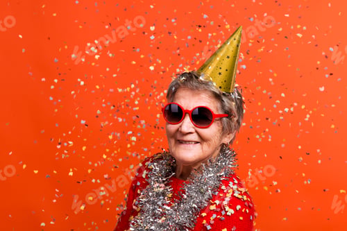 Preview: Portrait of a senior woman in studio on a red background. Party concept.