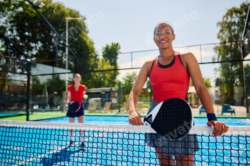 Preview: Happy black athletic woman playing padel with friends and looking at camera.