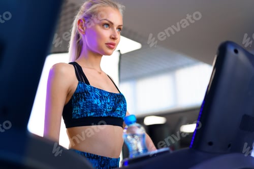 Preview: Young sports woman is working out in gym. Doing cardio training on treadmill