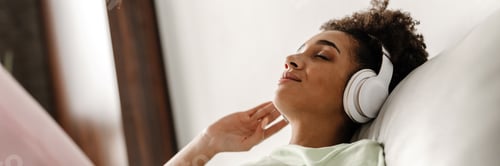 Preview: Young black woman listening music with headphones while sitting on couch