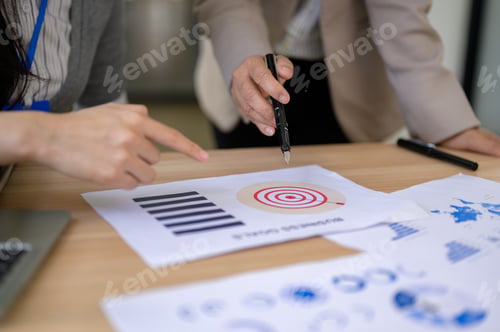 Preview: Close up of businesswoman's hand pointing pen at document on wooden table aside coworker in office.