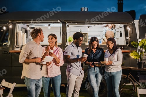 Preview: Multiethnic friends resting outside food truck in evening