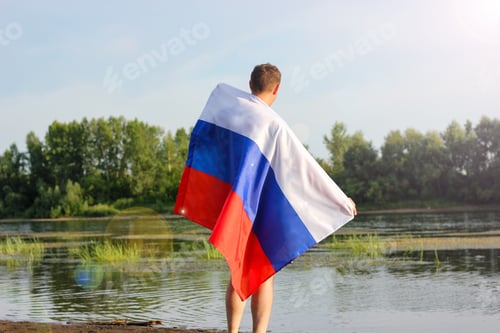Preview: a man stands on the bank of the river with the flag of Russia from three stripes white blue and red