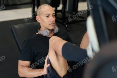 Preview: Hispanic bald man athlete in gym doing leg press