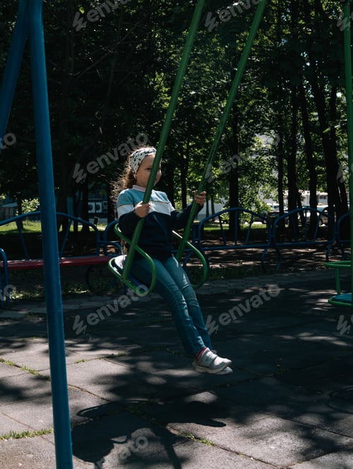 Preview: Happy child on a swing in sping park on vacation. Cute little girl with long blond hair swinging