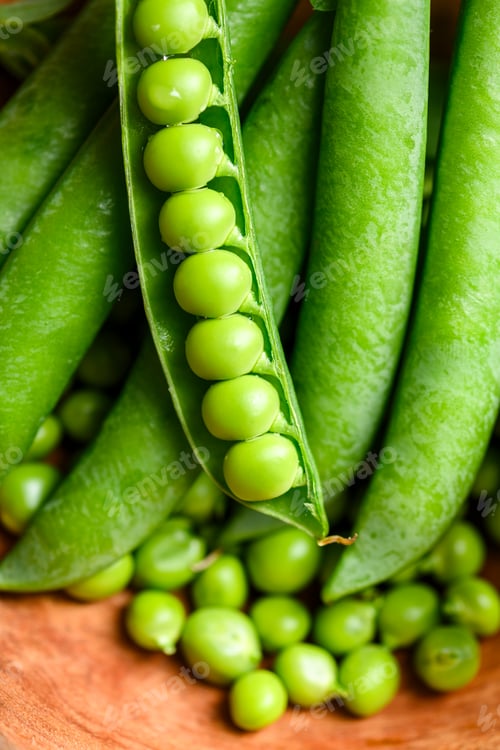 Preview: Green peas overflowing from wooden bowl with pods
