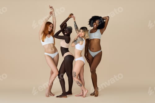 Preview: Happy interracial girls wearing underwear dancing together on beige background.