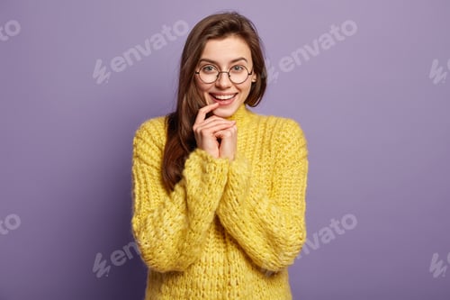 Preview: Waist upp shot of smiling cute lady keeps hand near mouth, rejoices good day, wears round spectacles