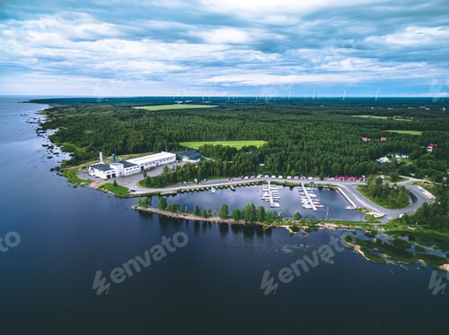 Preview: Aerial view of nordic summer landscape with blue sea and green forest with windmills on the horizon.