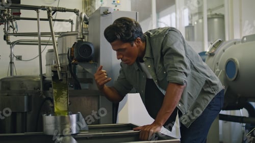 Preview: Professional guy tasting olive oil at factory close up. Man controlling process