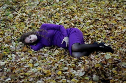 Preview: Pregnant woman lying in fetal position on autumn leaves loneliness, fear for the future of the child
