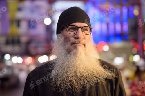 Preview: Face of mature bearded tourist man with eyeglasses thinking in Chinatown at night