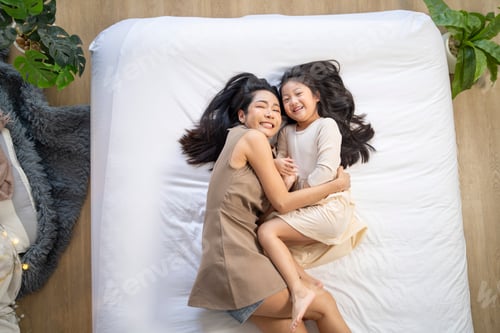 Preview: mother and daughter laughing together while lying on a bed