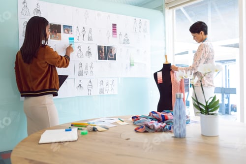 Preview: Rear view of beautiful diverse female fashion designers working in a modern office