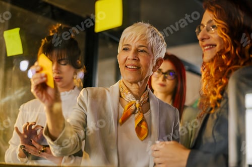 Preview: Female creative innovative team writing business plan on sticky notes.