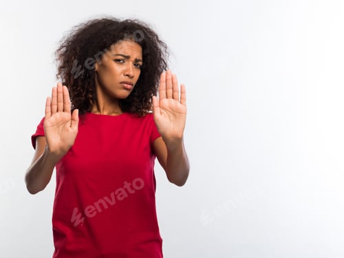Preview: Portrait of serious young african woman in red t-shirt showing stop gesture with palms over white