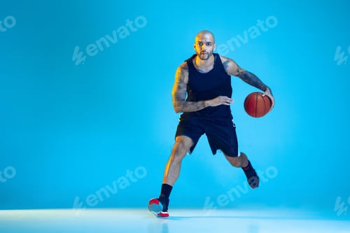 Preview: Young basketball player training isolated on blue studio background in neon light
