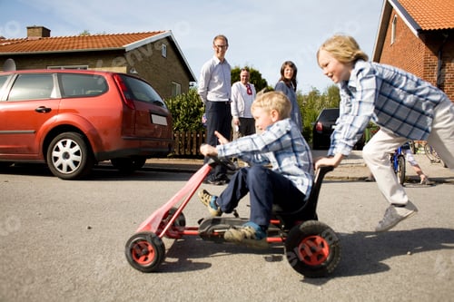 Preview: Boy pushing brother on quadricycle against family in background