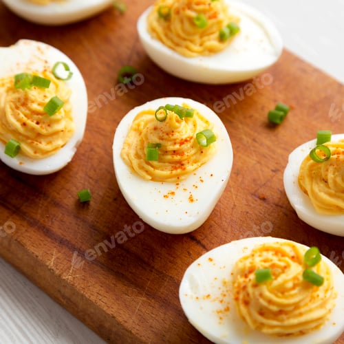 Preview: Homemade Deviled Eggs with Chives on a rustic wooden board on a white wooden surface.