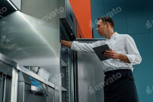 Preview: Professional chef using tablet computer for recipes while working in modern kitchen cooking concept