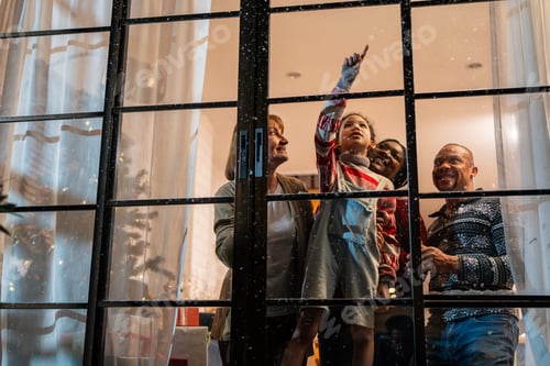 Preview: Adorable child looking at the window and first snow flakes with family.