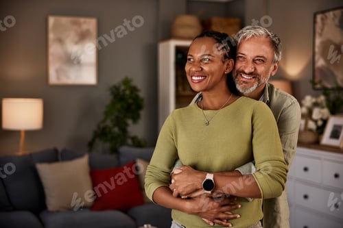 Preview: Mature man and an African woman hugging while standing in the living room.