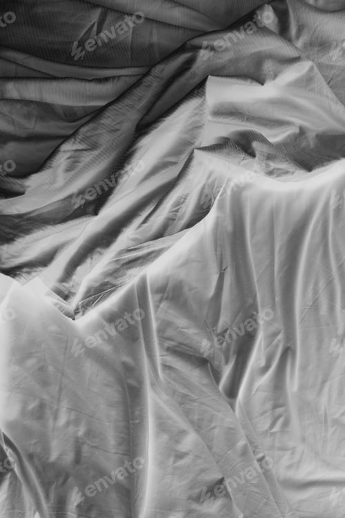 Preview: Black and white close up of wrinkled cotton sheets on bed.