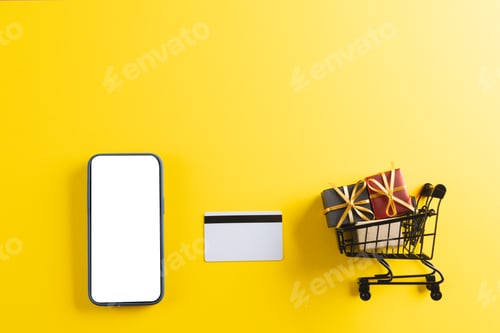 Preview: Credit card smartphone with copy space and trolley with gifts on yellow background