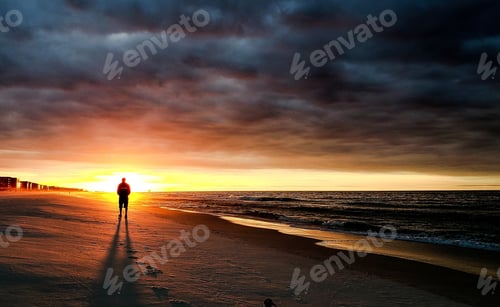 Preview: Silhouetted man standing on the beach watching the sunrise in the east in minimalism at sea.