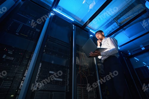 Preview: IT technician analyzing data from laptop in server room