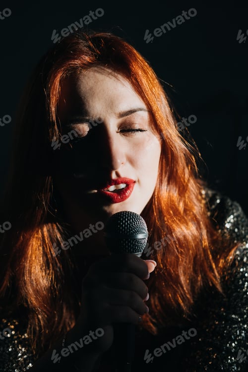 Preview: Portrait of redhead female singer woman in sparkly evening dress holding microphone on dark night