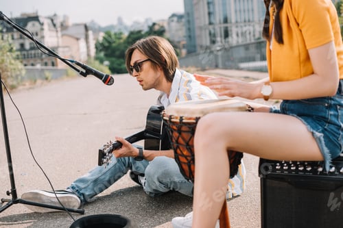Preview: Young happy female drummer and male guitarist at city street