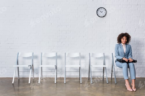 Preview: Smiling woman with briefcase waiting for interview while sitting on chair