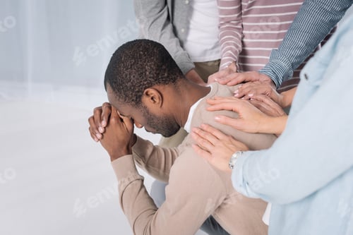 Preview: cropped shot of people supporting depressed african american man during group therapy