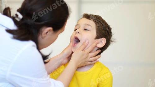 Preview: Otorhinolaryngologist doctor examining throat of little boy using spatula in clinic.