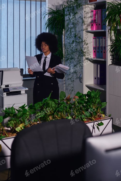 Preview: african american businesswoman with documents near copier and decorative plants at night in office