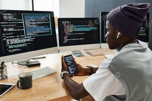 Preview: Young serious IT engineer in earphones scrolling through coded data