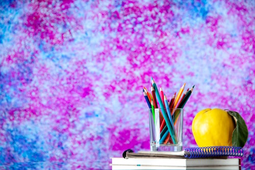Preview: Front view of colored pencils kept in a glass jar and quince with stem on stacked spiral notebooks