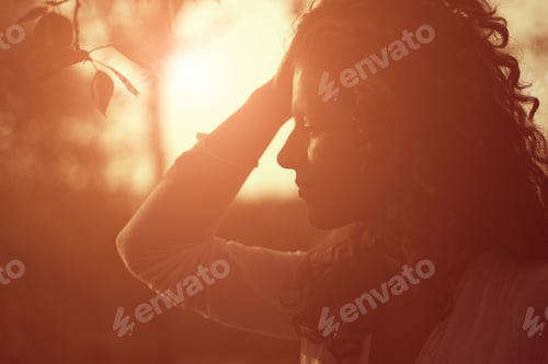 Preview: Portrait of a young beautiful girl with curly hair at sunset. Silhouette at sunset.