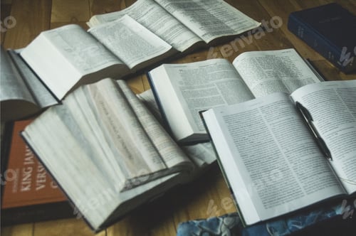 Preview: Closeup shot of opened books with a pen and the holy bible on the side on a wooden surface