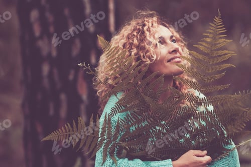 Preview: Portrait of happy cheerful woman holding big leaf in the forest with trees in background