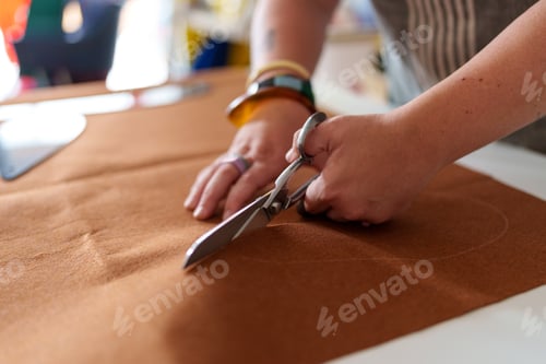 Preview: Skilled hands cutting brown fabric with scissors at wooden workspace