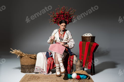 Preview: full length of ukrainian woman in traditional clothes and red floral wreath holding knitting needles