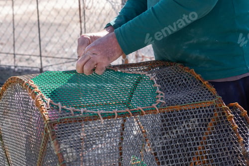 Preview: Close-up of the hands of elderly fisherman in the harbor dock as he repairs fishing nets using rope.
